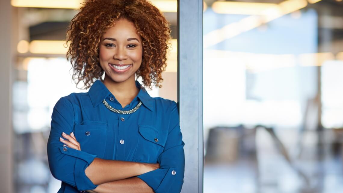 A woman smiles and leans against a glass door frame.