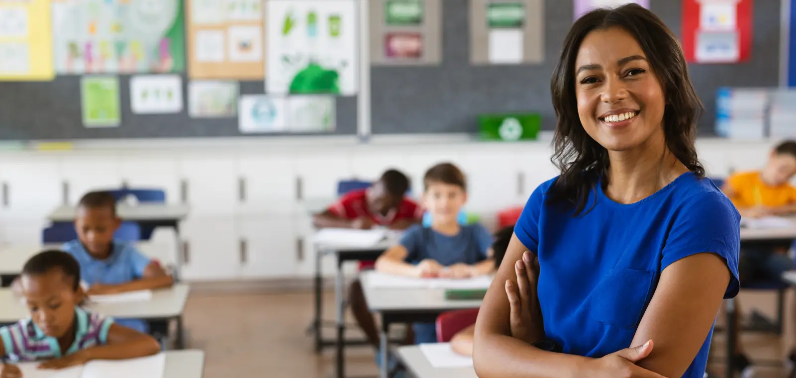 A teacher standing with her arms folded in front of a classroom.