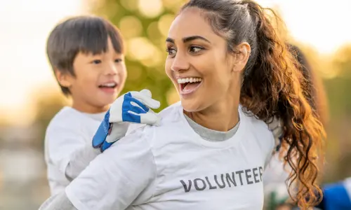 A woman wearing a white t-shirt carrying a young boy on her back.