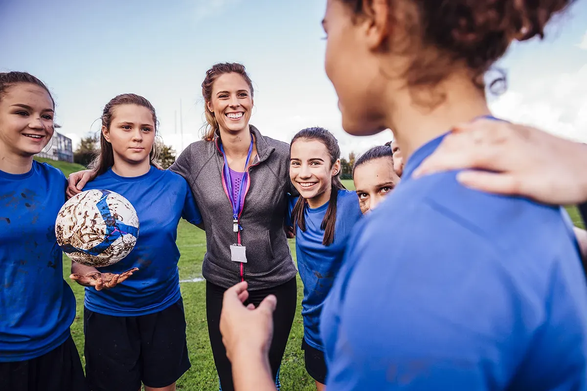 A female youth soccer team circles up around their volunteer coach for a pep talk on a soccer field. Learn about volunteer training requirements.