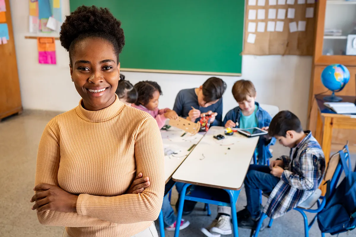 A teacher posing with her arms folded. There is a group of students in the background.