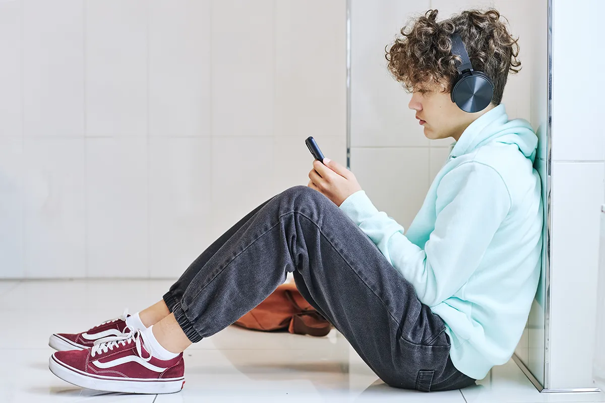 A depressed teenage boy holding a smartphone is a victim of online child sexual exploitation.