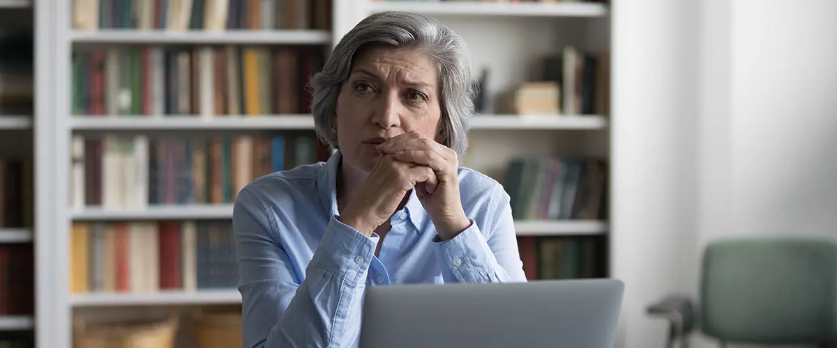 A professional woman sits at a computer, looking pensive.