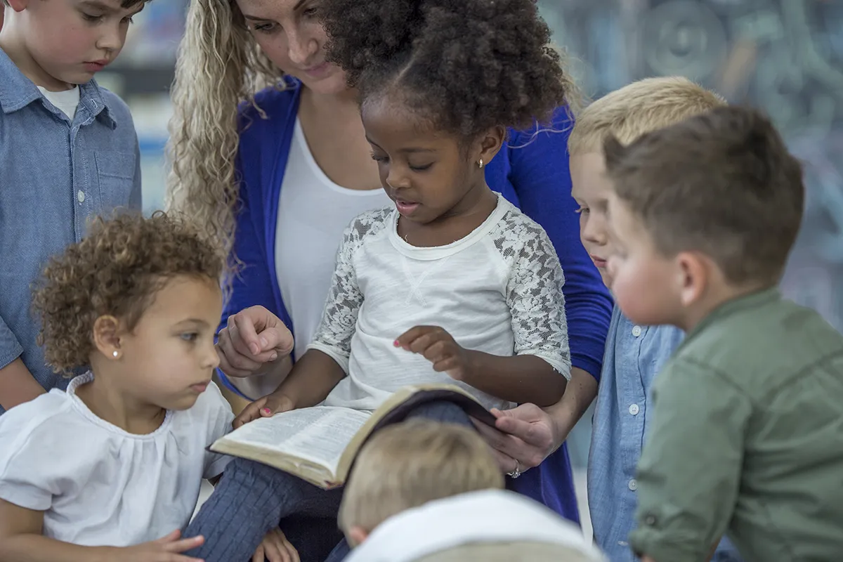 A female Sunday School teacher surrounded by children sits with a Bible on her lap. Find out how mandated reporting laws impact churches.