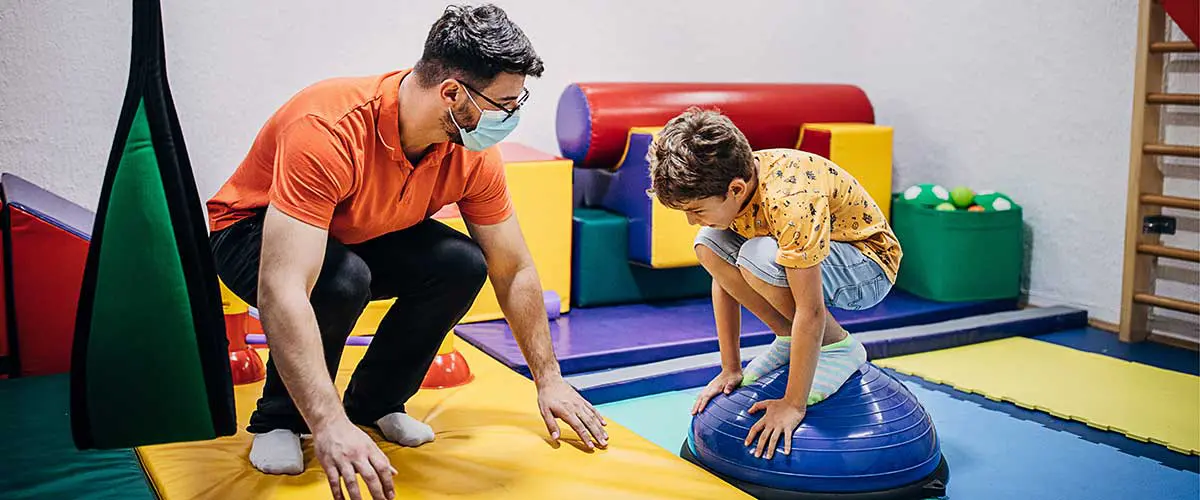 A child exercising with a physical therapist in a colorful room.