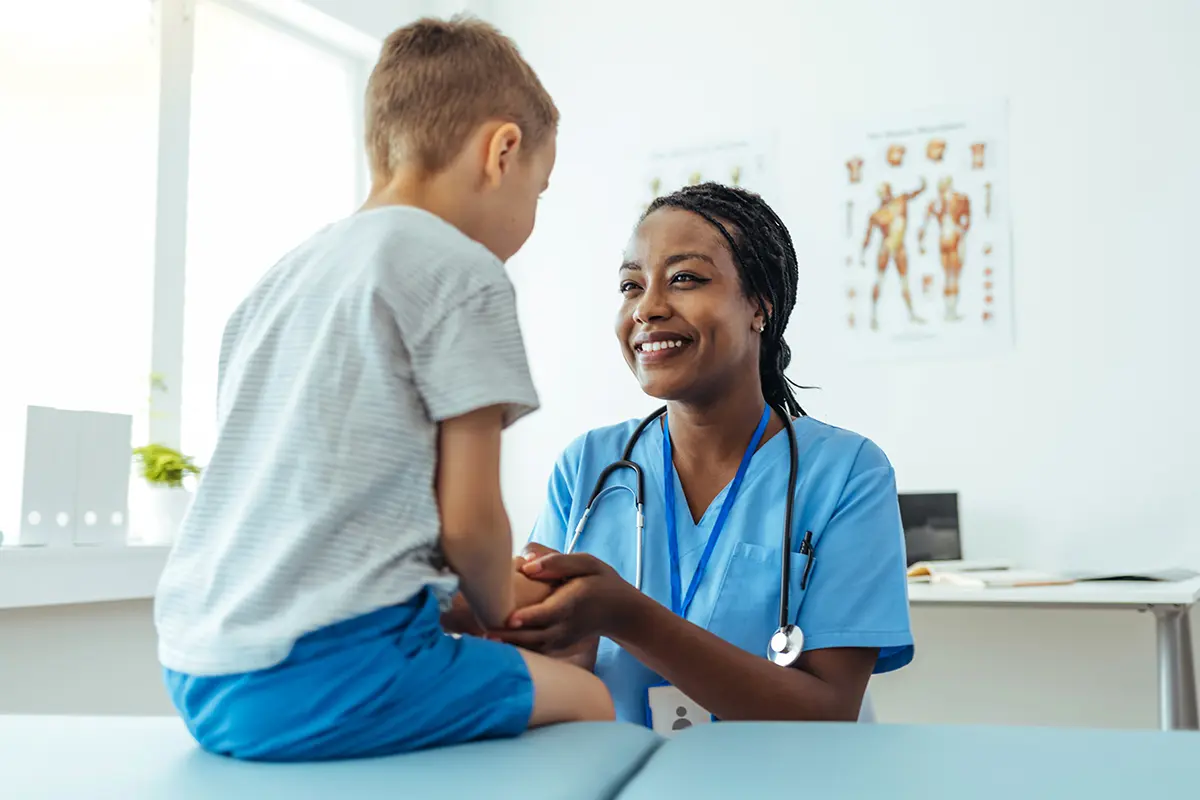 A female Black medical professional is smiling and treating a young patient. Find out what the mandatory reporting training requirements are for nurses.
