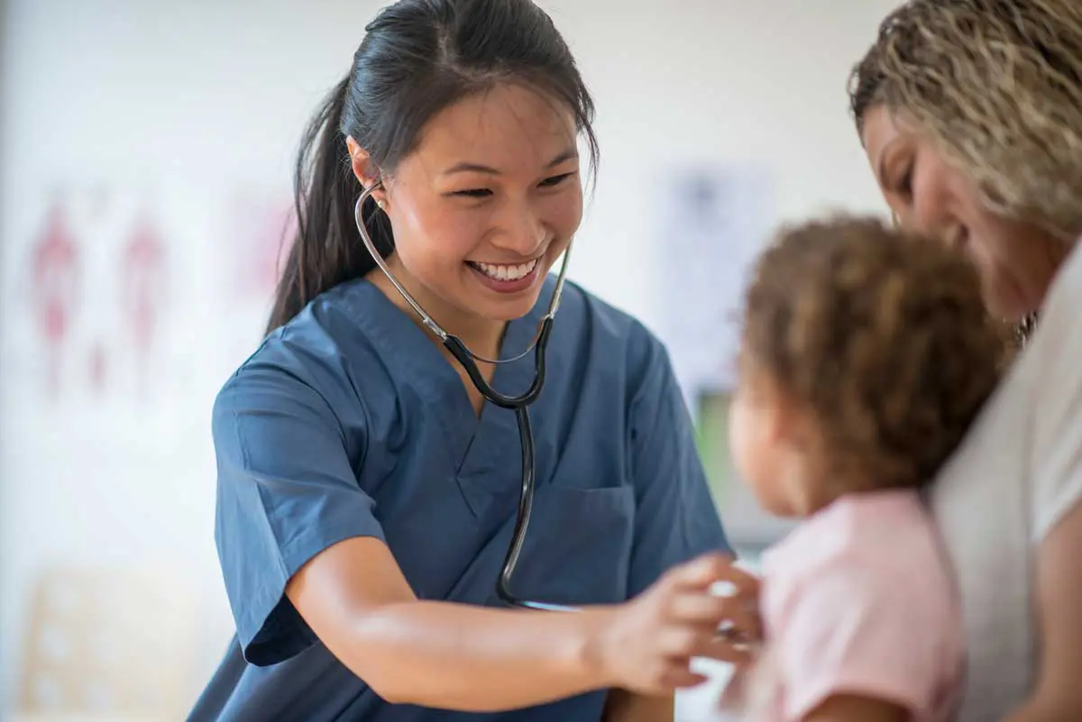 A female nurse smiling as she assesses a young child. Find out what nurses are responsible for reporting.