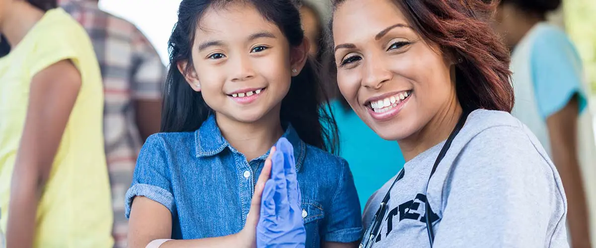 Image of smiling medical professional volunteering their time and giving happy little girl a high-five.