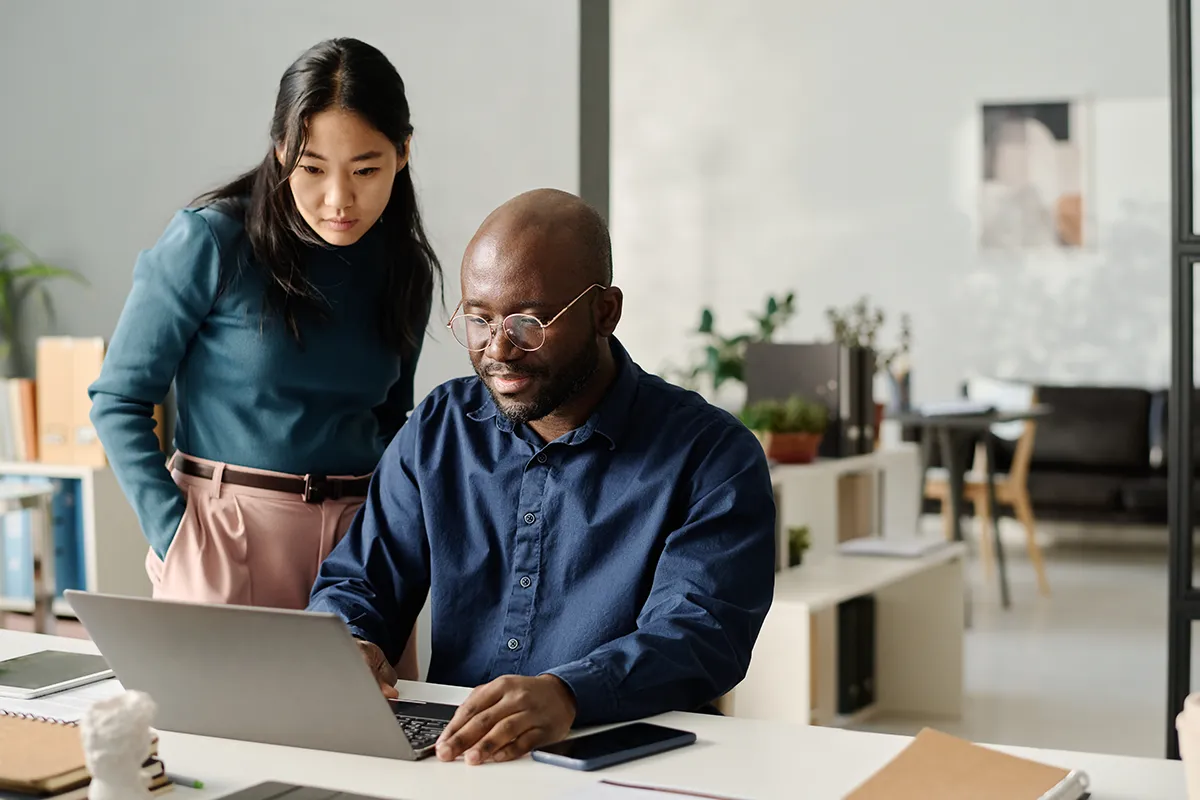 Two employees are in an office looking at a laptop screen while taking online employee training. Find out what to include in a CA employee training program.